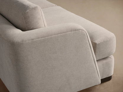A beige, three-seater Kayden Sofa with clean lines, plush cushions, and slightly curved armrests, on a wooden floor.