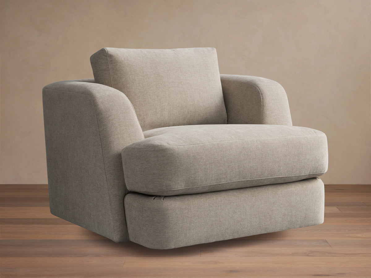 Kayden Swivel Chair with a beige fabric, plush seat, and back cushion. Features subtle rounded armrests and a sturdy swivel base on wooden floor.