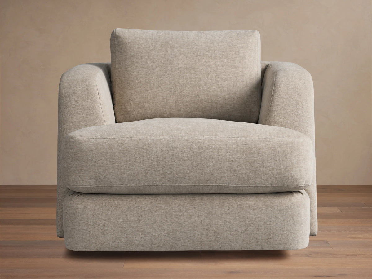 Kayden Swivel Chair with a beige fabric, plush seat, and back cushion. Features subtle rounded armrests and a sturdy swivel base on wooden floor.