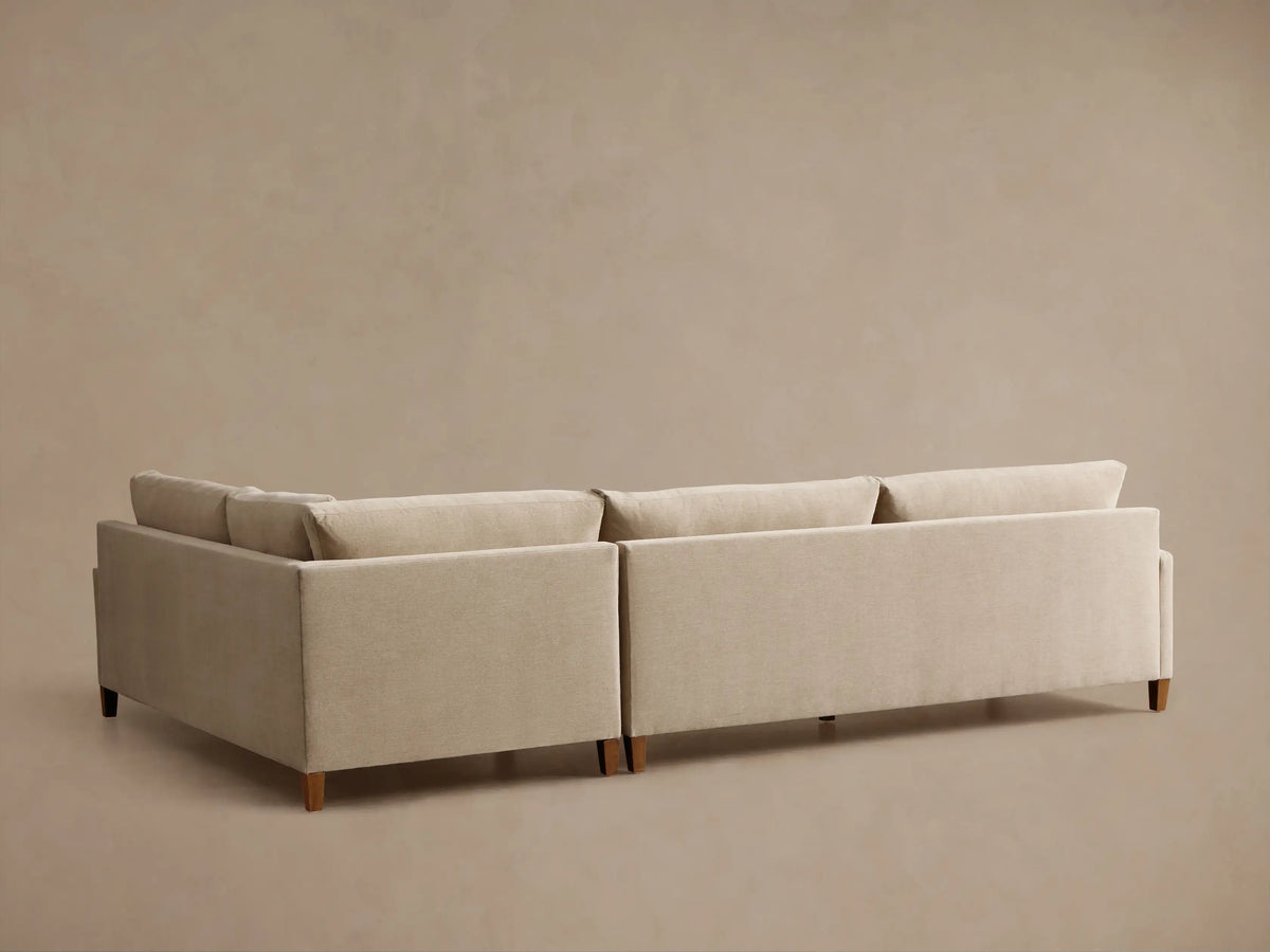 Close-up of the beige Kipton Slim Arm Elevated Two-Piece Sectional, showing the corner cushions, slim arm, and a mocha finish leg.