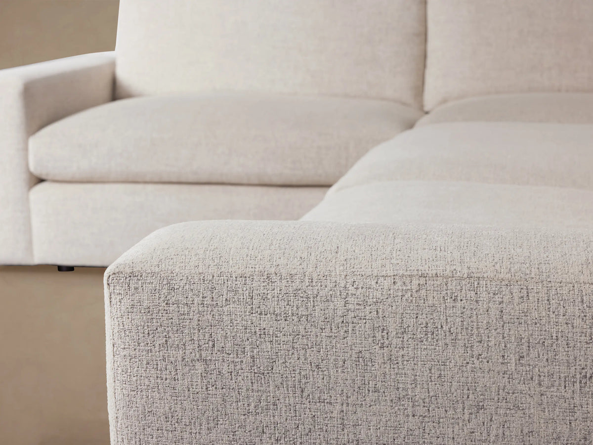 Kipton Wide Arm Two-Piece Sectional, L-shaped, light beige fabric, with wide square arms, on a wooden floor against a beige wall.