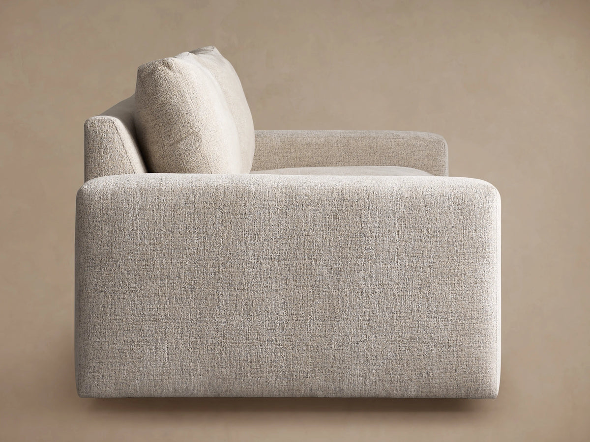 Kipton Wide Arm Sofa in textured light beige fabric, showing the wide armrest, seat, and back cushions from an angle.