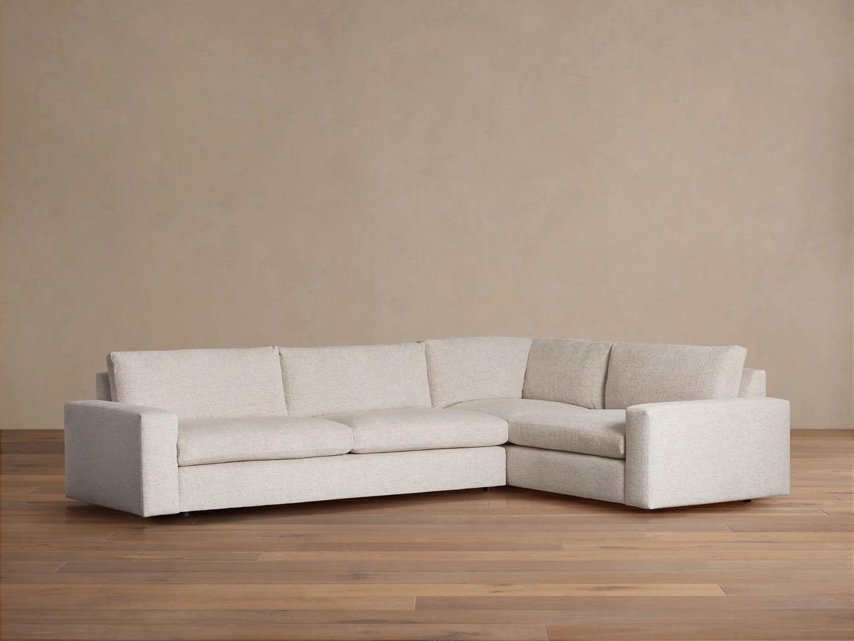 Light beige Kipton Wide Arm Two-Piece Sectional, L-shaped, with wide arms and low profile base, on a wood floor.