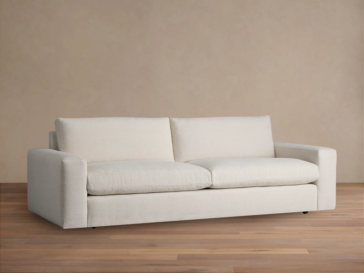 Front view of Kipton Wide Arm Sofa, cream textured fabric, with wide block arms and 2 plush seat cushions, on a wooden floor.