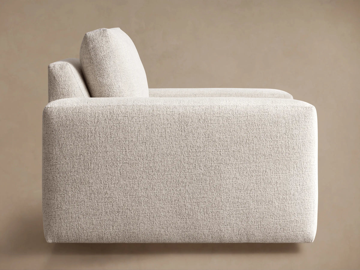 Kipton Wide Arm Swivel Chair in light beige textured fabric, seen from a three-quarter rear view, showing wide block arms.