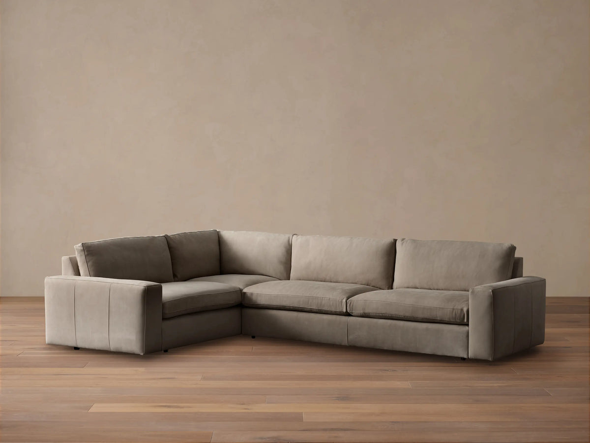 Kipton L-shaped, two-piece, wide-arm sectional sofa in light taupe nubuck leather with plush cushions, against a neutral wall.