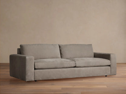 Kipton wide arm nubuck leather sofa in light taupe, with two seat/back cushions, on wood floor, against a beige wall.