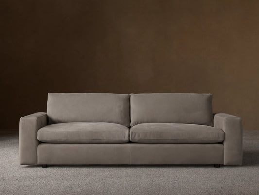 Kipton wide arm nubuck leather sofa in light taupe, with two seat/back cushions, on wood floor, against a beige wall.