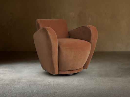 Front-right view of a plush, curved, rust-colored velvet Amelia Swivel Chair on a black swivel base, set on a wooden floor.
