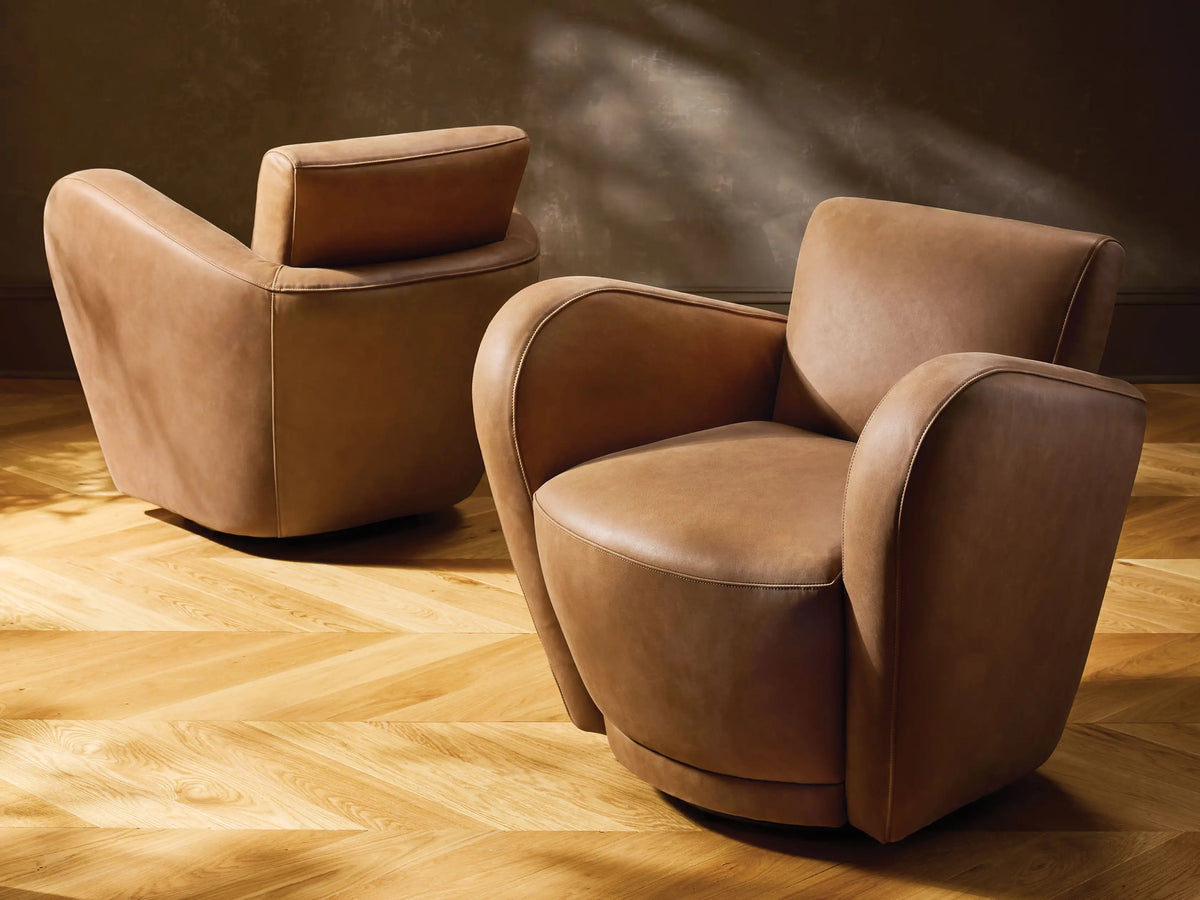 Two tan leather Amelia Swivel Chairs. The foreground chair faces right, the background chair shows its back, on a wood floor.
