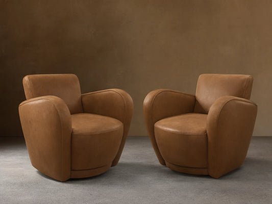 Two tan leather Amelia Swivel Chairs. The foreground chair faces right, the background chair shows its back, on a wood floor.