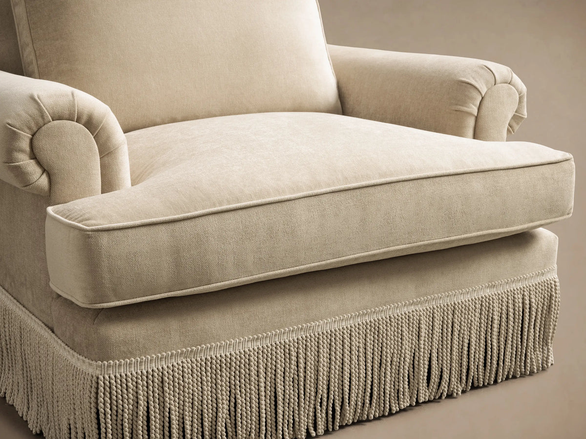 Close-up of the light beige McKinley Chair with Fringe, showing an angled view of the armrest and back cushion upholstery.