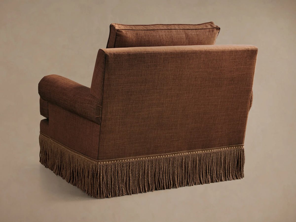 Close-up of the brown textured fabric on the rolled arm with pleated detail and the back cushion of the McKinley Chair with Fringe.