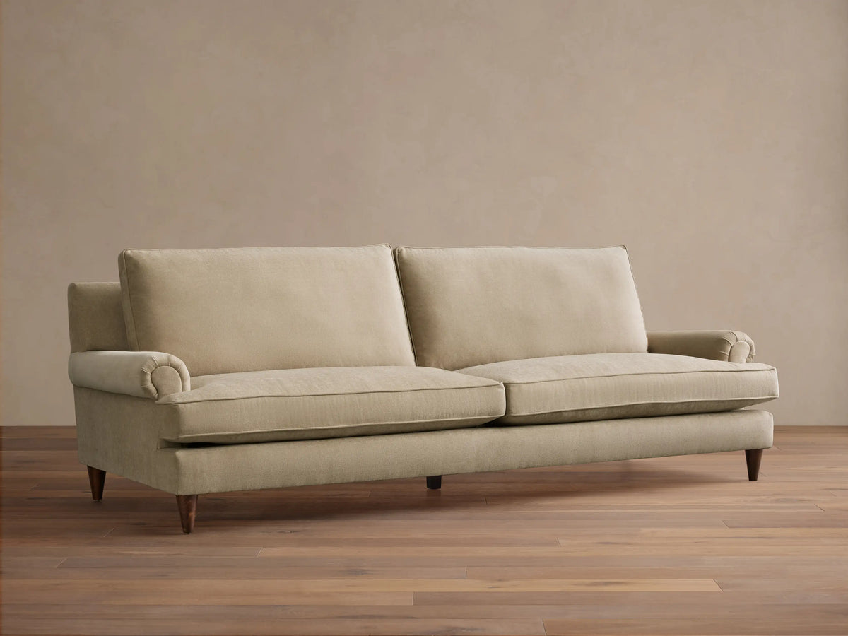 Rear three-quarter view of the light beige McKinley Sofa, showing its upholstered back, two back cushions, and tapered wooden legs.