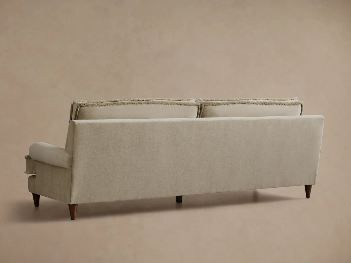 Rear view of the light beige McKinley Sofa with fringed back cushions and dark wooden legs.