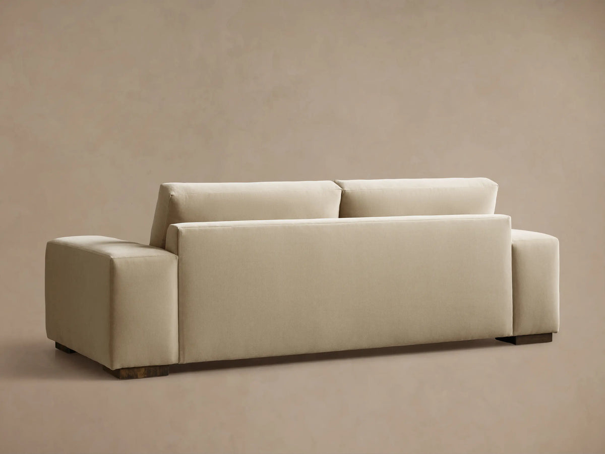 Rear view of the cream Madson Sofa with square arms and dark wooden feet, angled left.