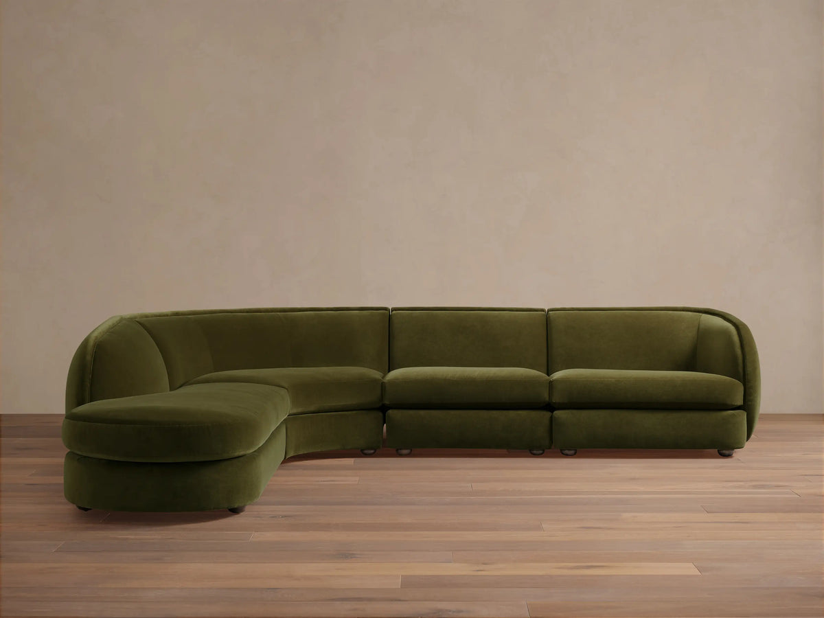 Olive green Milana Four-Piece Bumper Sectional on wooden floor, featuring armless chair, corner wedge, and arm chairs in a crescent shape.