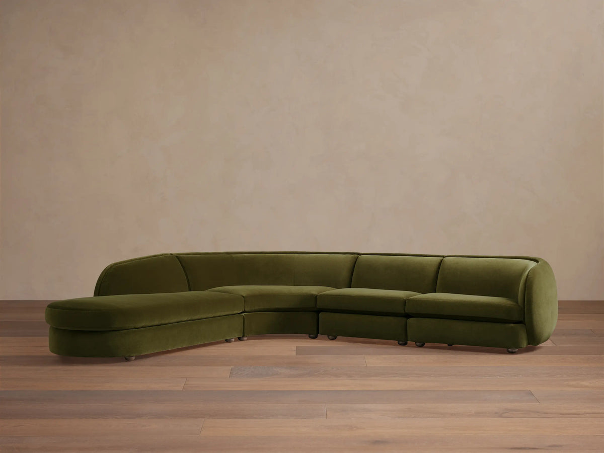 Olive green Milana Four-Piece Bumper Sectional on wooden floor, featuring armless chair, corner wedge, and arm chairs in a crescent shape.
