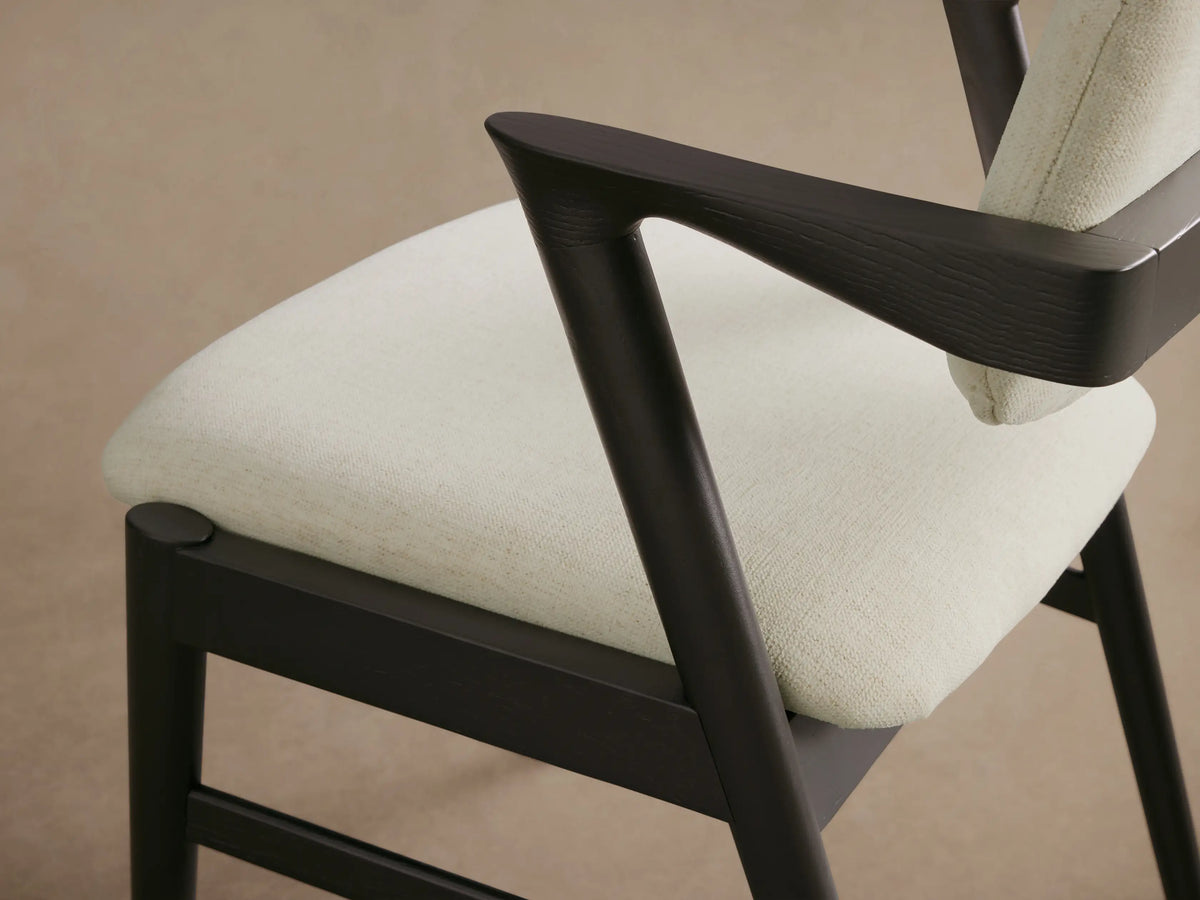 Marais Dining Arm Chair, front view. Dark ash wood frame, light cream fabric upholstered seat and backrest, on wood floor.