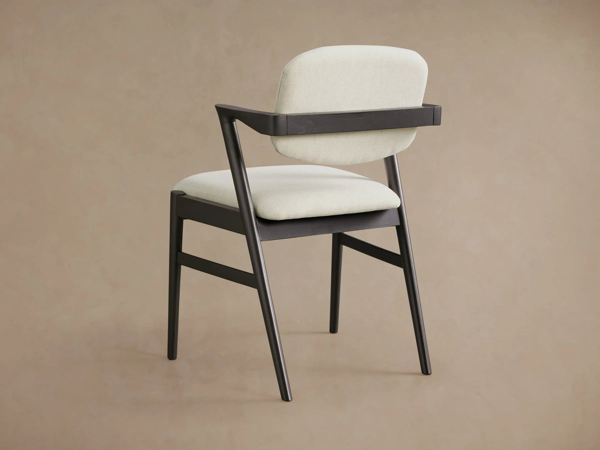 Close-up of Marais Dining Arm Chair: dark ash wood frame with light, textured fabric seat & backrest, prominent armrest.