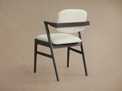 Close-up of Marais Dining Arm Chair: dark ash wood frame with light, textured fabric seat & backrest, prominent armrest.