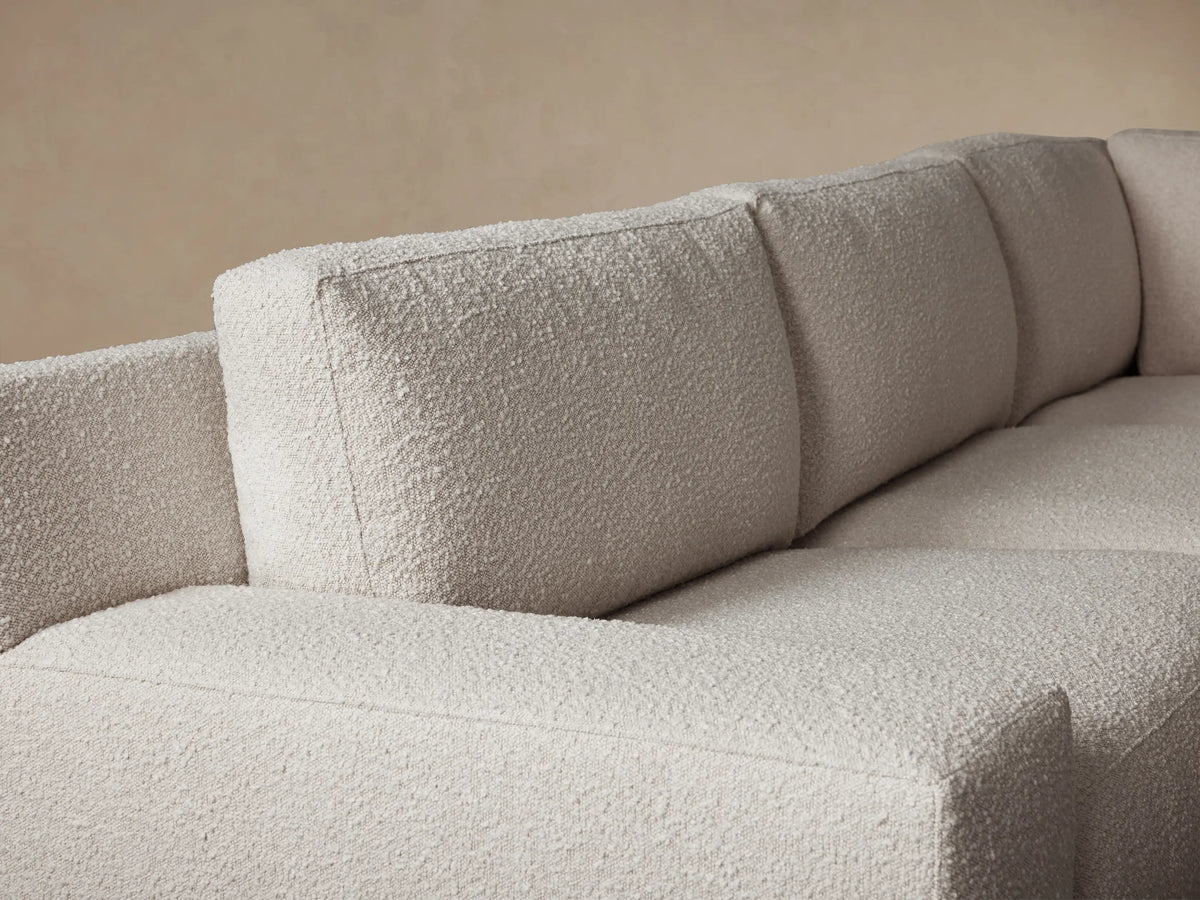 Novoli Four-Piece Chaise Sectional, large L-shaped, light oatmeal textured fabric. Right-hand chaise. Placed on a wooden floor against a beige wall.