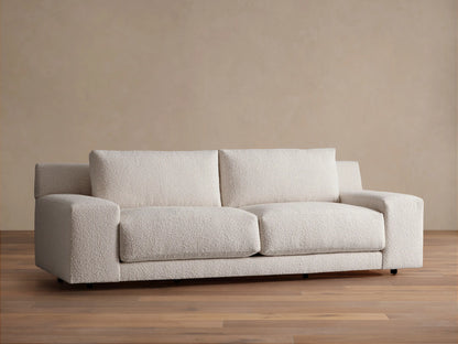 Novoli Sofa, cream boucle fabric, two seat cushions, square arms. Front view on a wood floor against a beige wall.