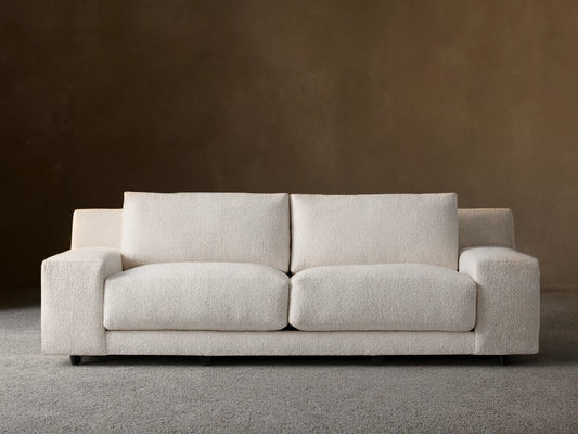 Novoli Sofa, cream boucle fabric, two seat cushions, square arms. Front view on a wood floor against a beige wall.