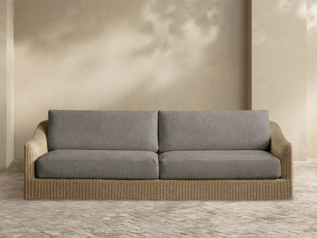 Front view of a two-seater outdoor sofa with grey fabric cushions and a light brown woven rattan base.