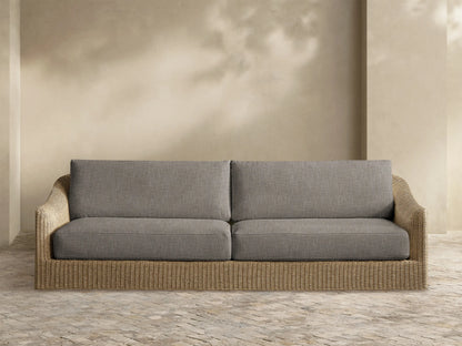 Front view of a two-seater outdoor sofa with grey fabric cushions and a light brown woven rattan base.