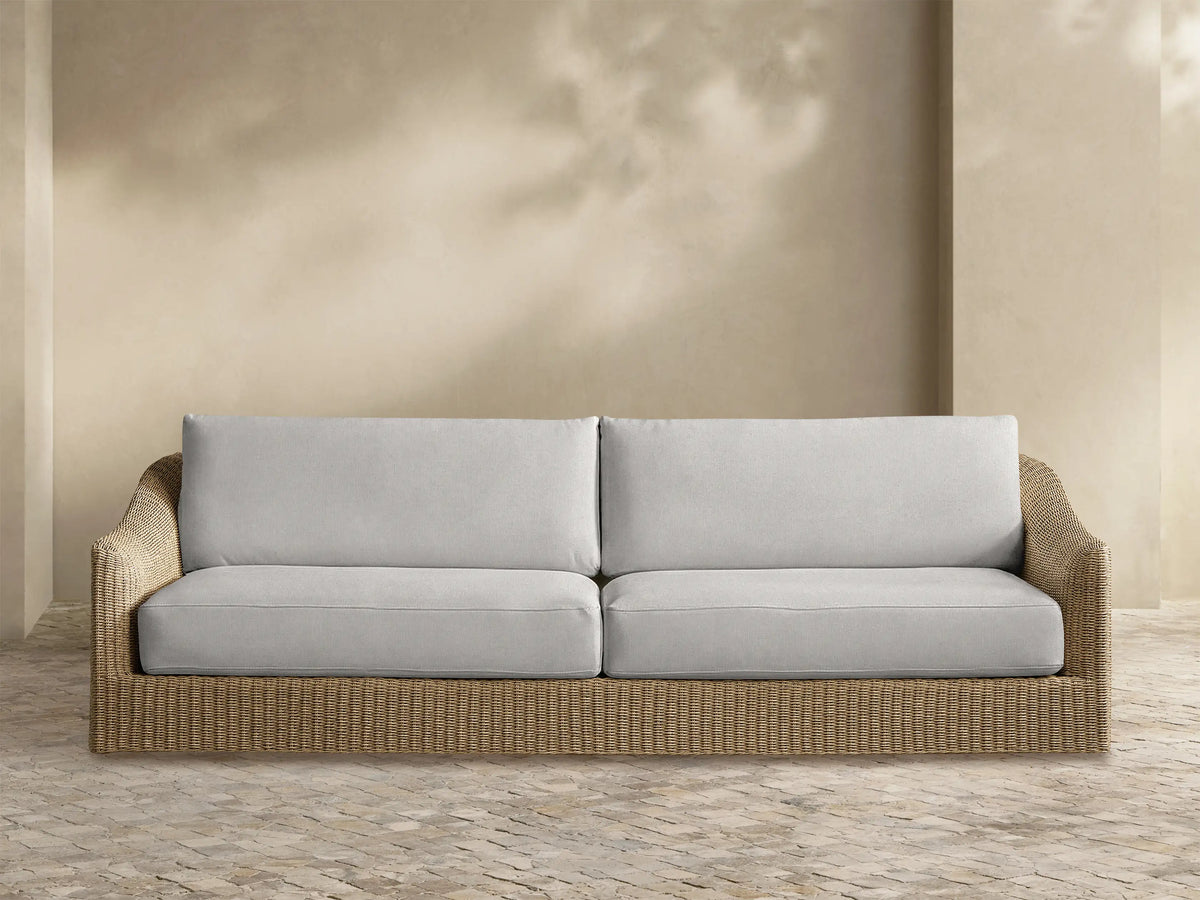 Front view of the Ancona Outdoor Sofa, featuring handwoven all-weather wicker and light gray cushions on a patio.