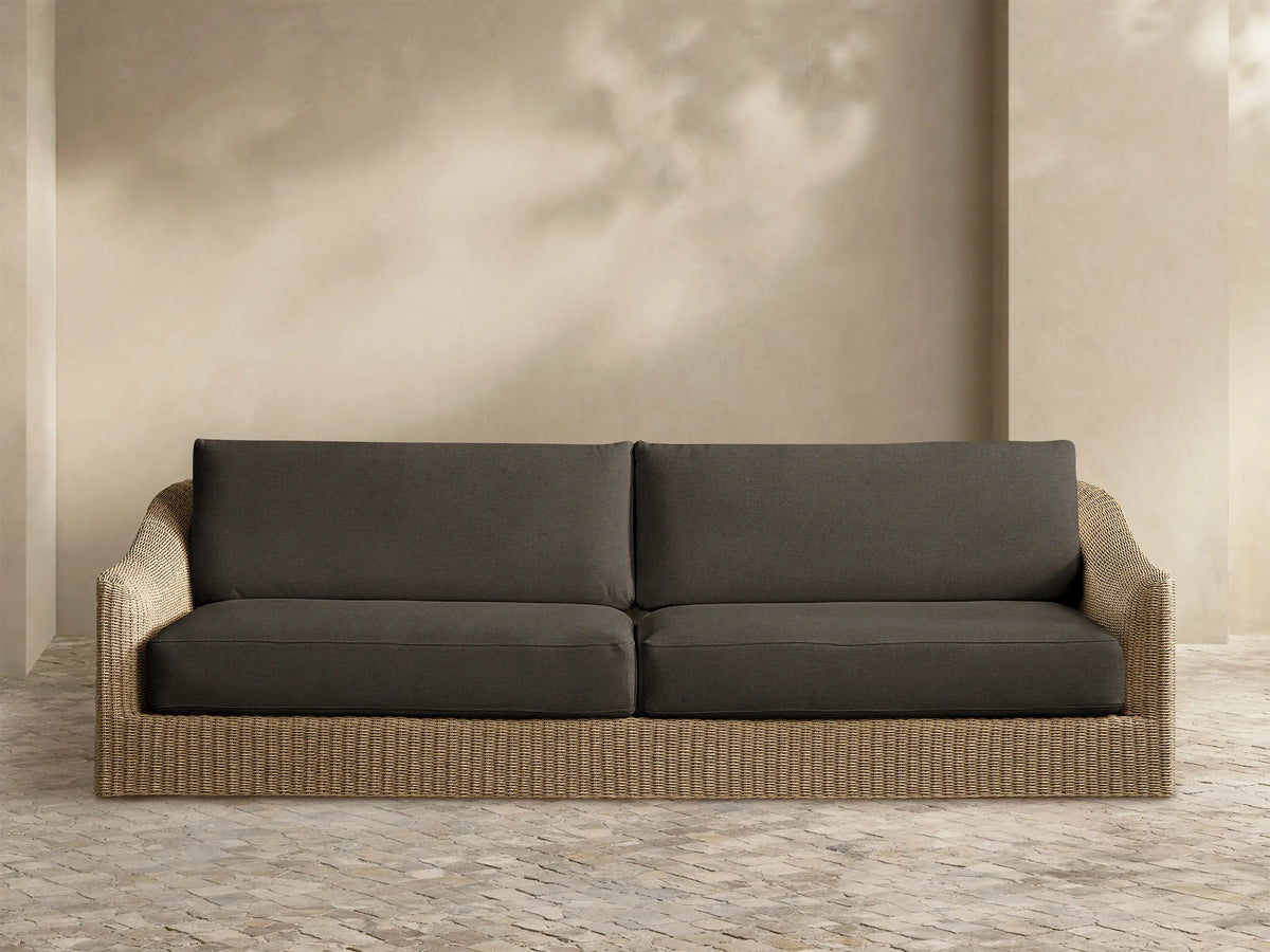 Front view of the Ancona Outdoor Sofa with a handwoven, light brown wicker frame and dark gray seat and back cushions.