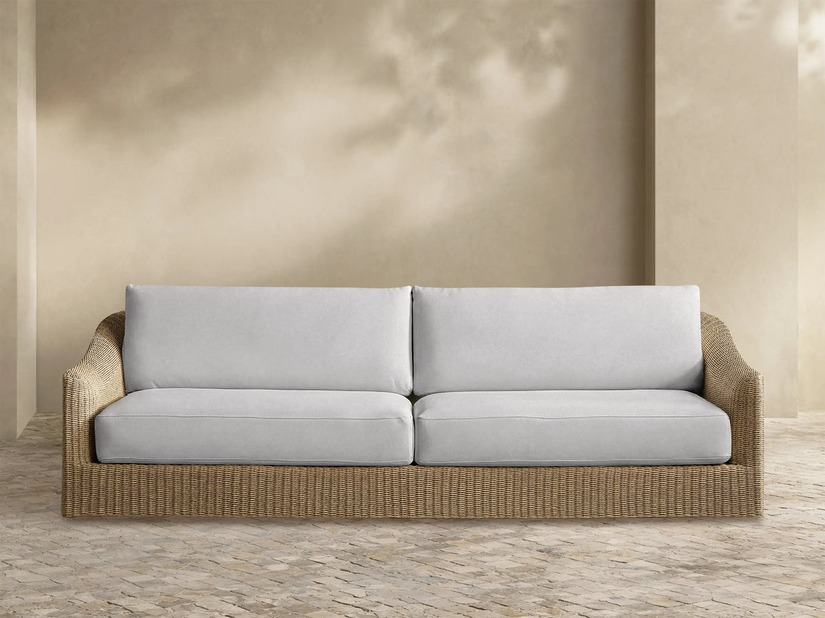 Front view of Ancona Outdoor Sofa with natural-toned handwoven all-weather wicker frame, curved arms, and light gray cushions.