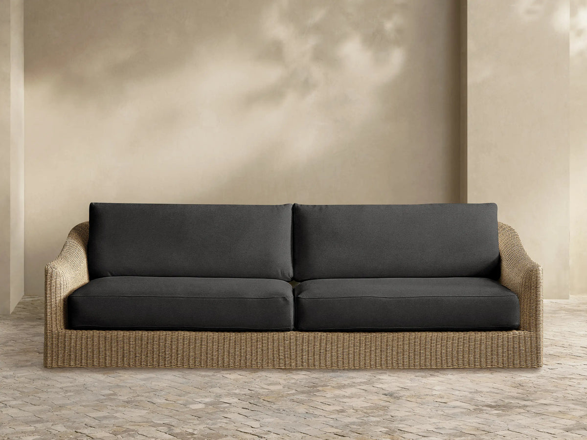 Front view of Ancona Outdoor Sofa with dark grey cushions and a light brown, handwoven wicker frame.