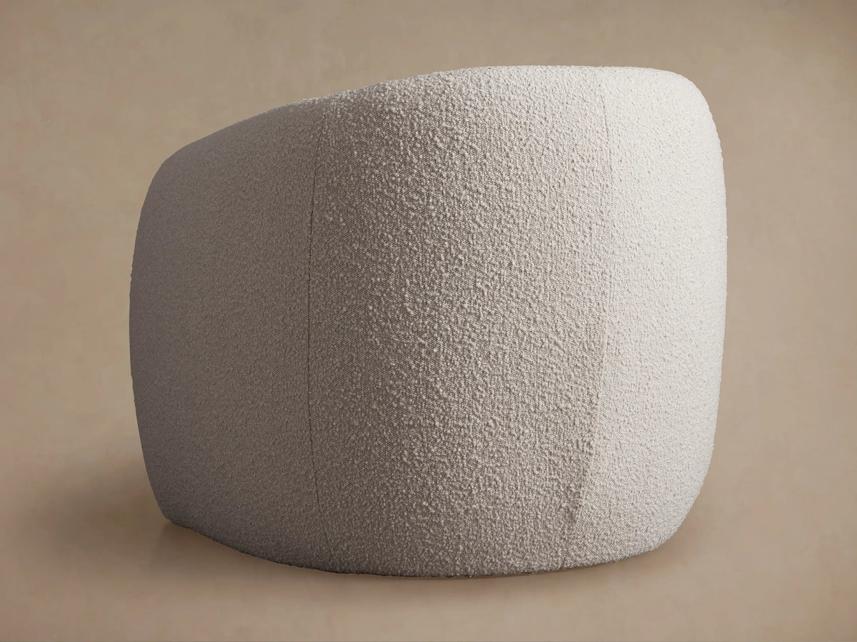 Close-up of a rounded, cream bouclv© Fresno Floating Seat Chair with a distinct floating seat design against a beige wall.