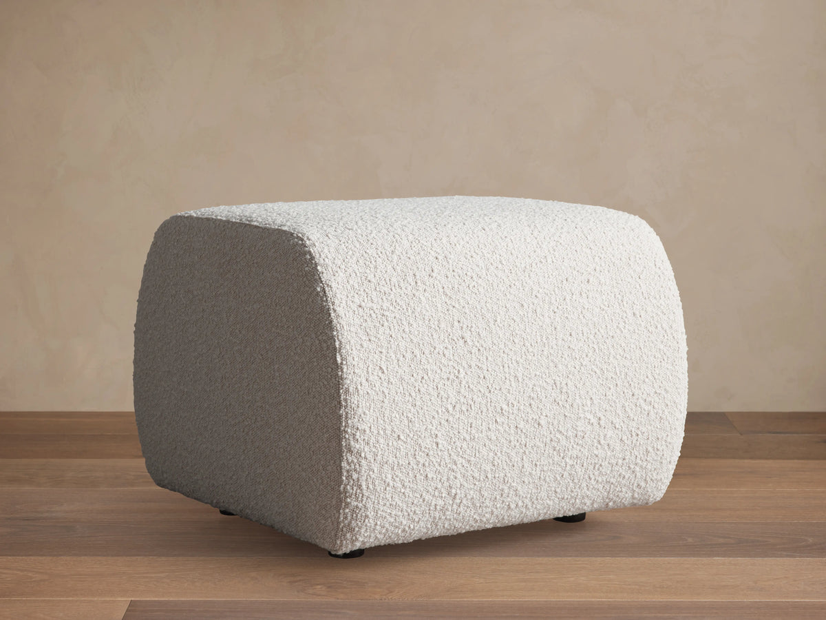 Square Fresno Ottoman featuring a beige, brown, and gray woven checkered pattern, positioned on a light rug.