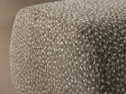 Fresno Ottoman in textured gray fabric with a rounded rectangular shape. Sits on short black legs, placed on wooden floor.