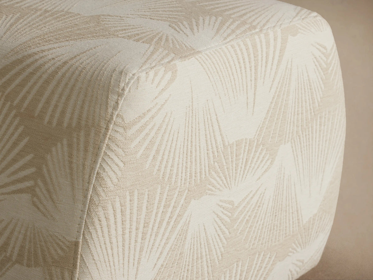 Fresno Ottoman: Square, off-white upholstered with rounded edges and a subtle cream fan pattern, shown on a wooden floor.