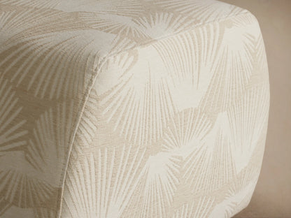 Fresno Ottoman: Square, off-white upholstered with rounded edges and a subtle cream fan pattern, shown on a wooden floor.