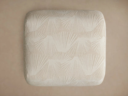 Close-up of a Fresno Ottoman, showing its light beige fabric with a subtle raised palm frond pattern on its corner and curved side.