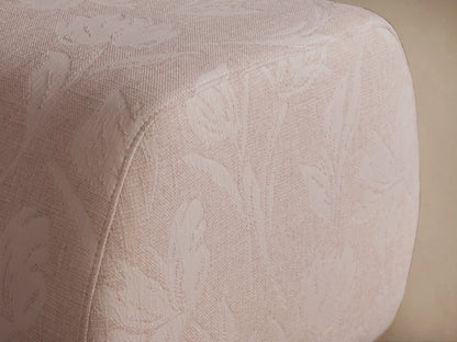 Fresno Ottoman: Light beige upholstered with subtle woven floral pattern, rounded edges, viewed at a slight angle on a neutral background.