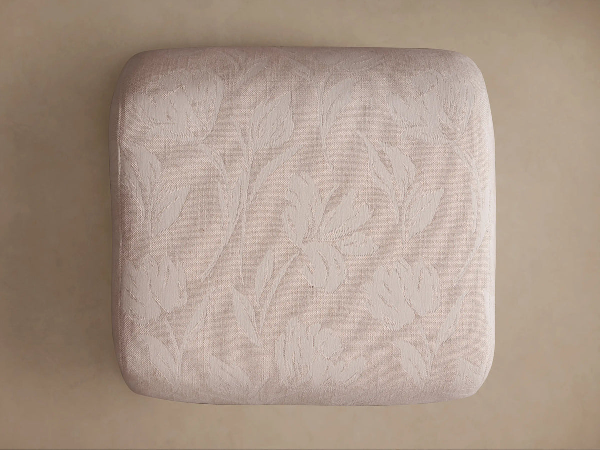Close-up of Fresno Ottoman's light beige textured fabric with subtle woven floral/leaf pattern on a rounded edge.