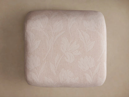 Close-up of Fresno Ottoman's light beige textured fabric with subtle woven floral/leaf pattern on a rounded edge.
