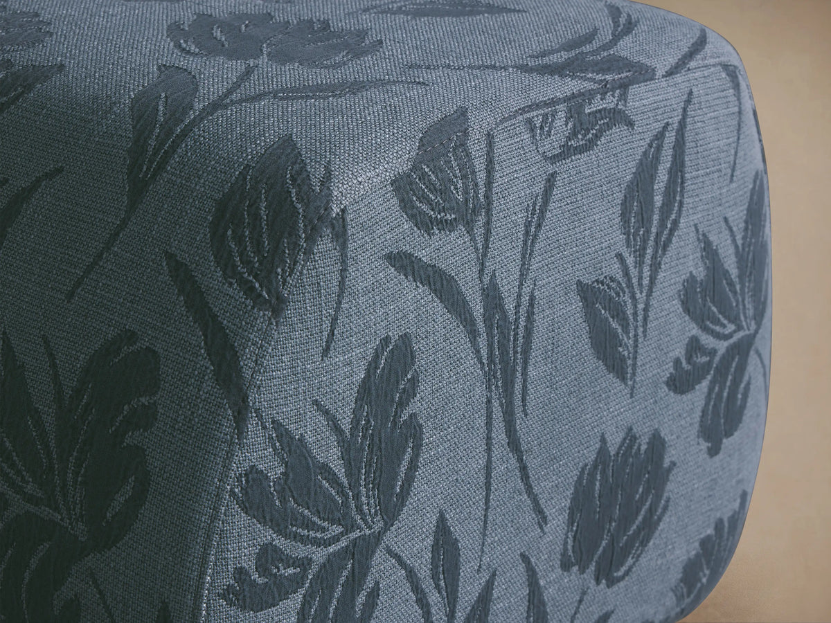 Fresno Ottoman: Rounded rectangular ottoman in light blue fabric with darker blue floral pattern, sitting on a wooden floor.