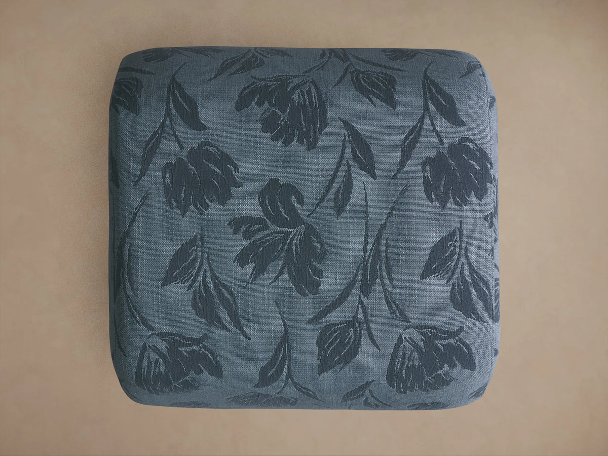 Fresno Ottoman close-up: blue-grey textured fabric with a darker, subtle embossed floral pattern of leaves and blooms.
