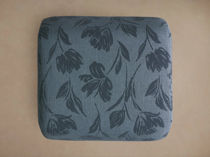 Fresno Ottoman close-up: blue-grey textured fabric with a darker, subtle embossed floral pattern of leaves and blooms.