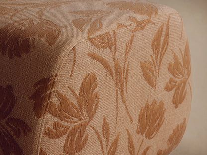 Fresno Ottoman, a rounded rectangular ottoman upholstered in beige fabric with a golden floral pattern, on a wooden floor.