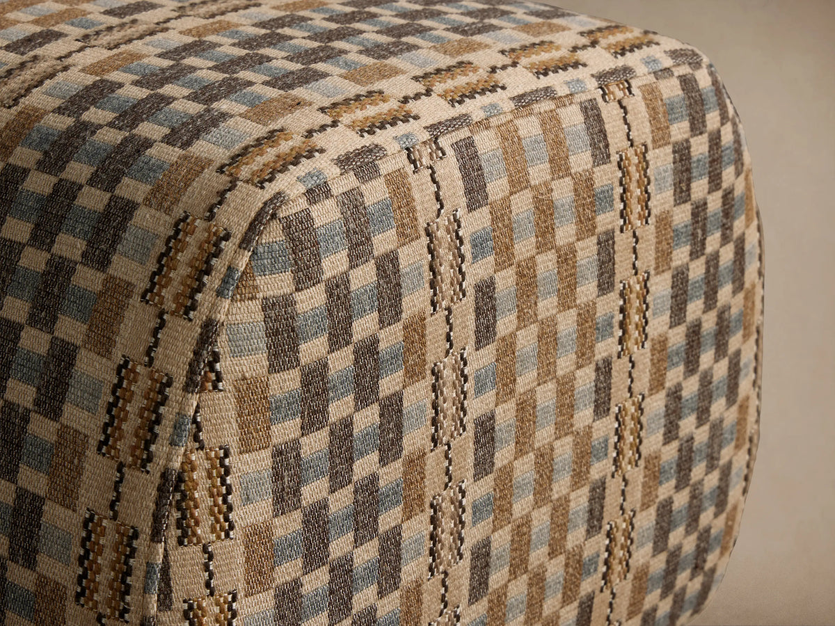 Fresno Ottoman: a rounded rectangular ottoman upholstered in a brown, beige, and blue geometric checkered fabric on a wooden floor.