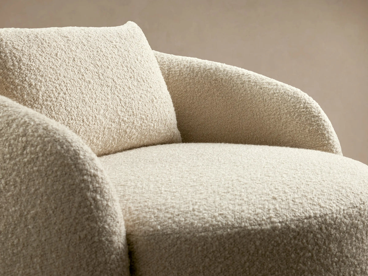 Oversized swivel chair in cream boucle fabric with a round seat, curved backrest, and matching cushion on a wooden floor.