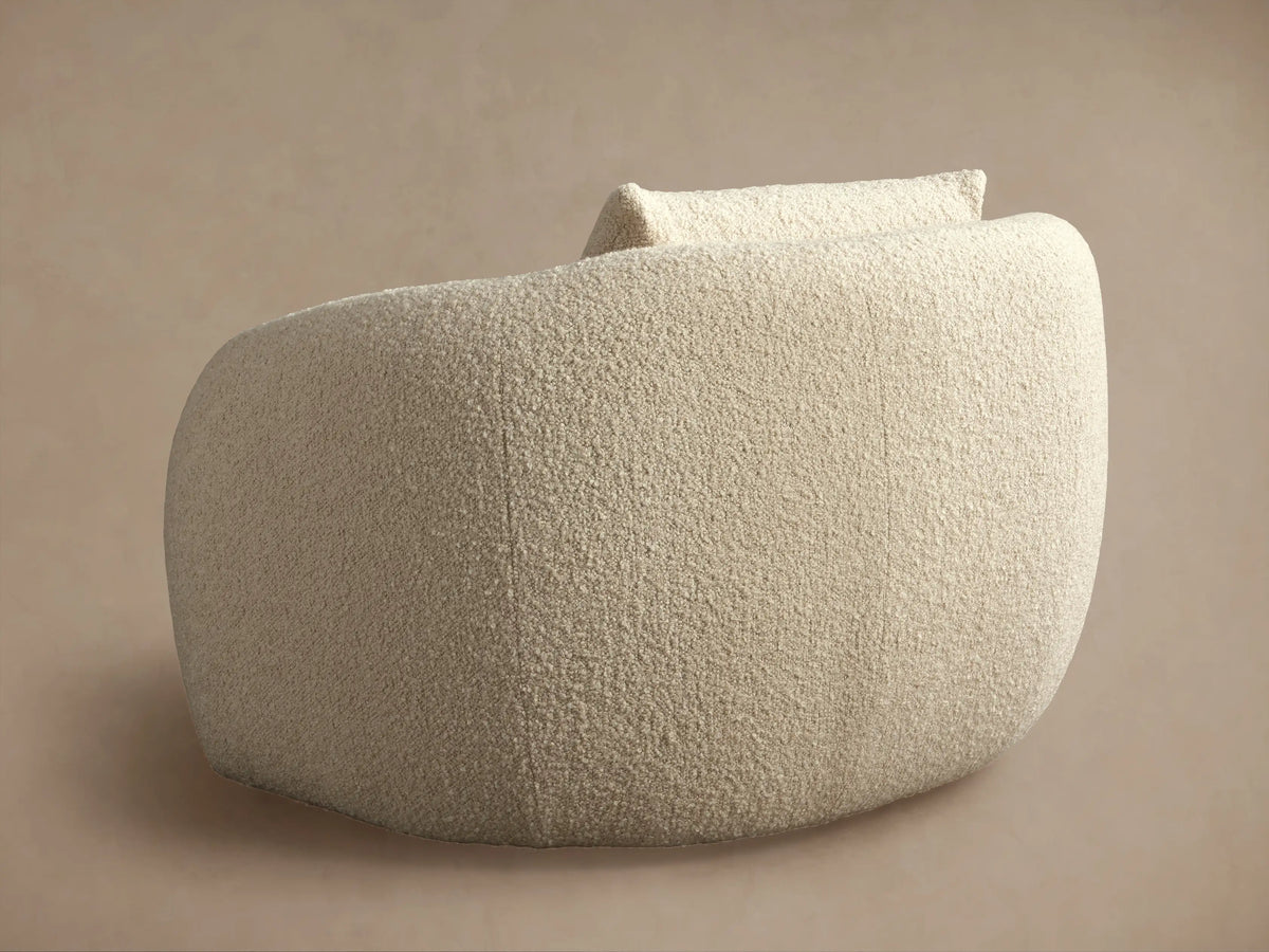 Fresno Oversized Swivel Chair in cream fabric, side view showing rounded back and seat. Soft texture, on a beige background.